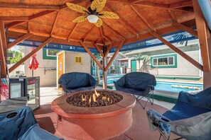An outdoor seating area with a fire pit, covered by a wooden structure with a leaf-shaped ceiling fan. - Aloha Springs! Private Heated Pool & Hot Tub (Colorado Springs)