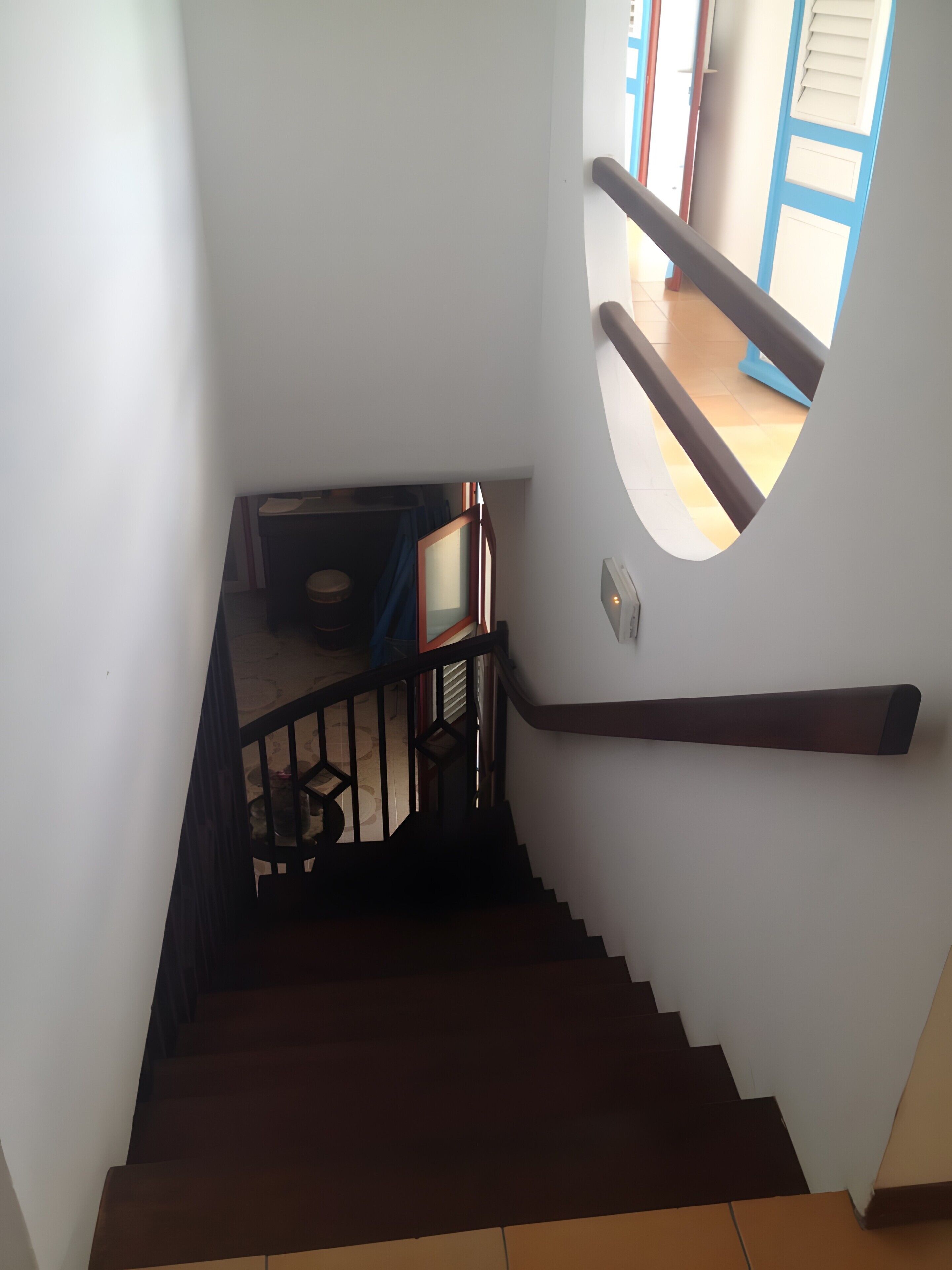 A staircase with a handrail and a circular window on the wall.