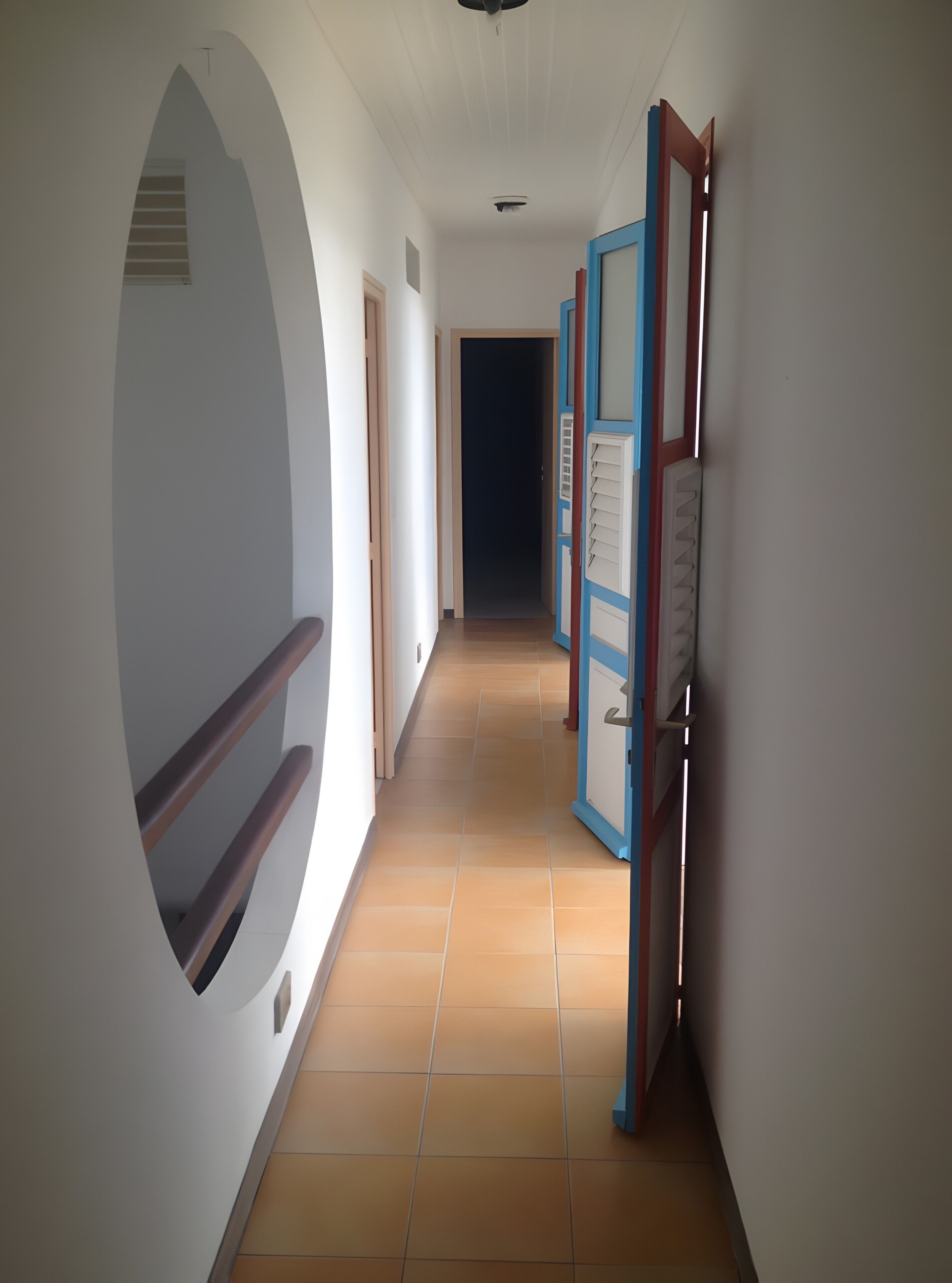 A corridor with a circular window, a door with a blue frame, and a tiled floor.