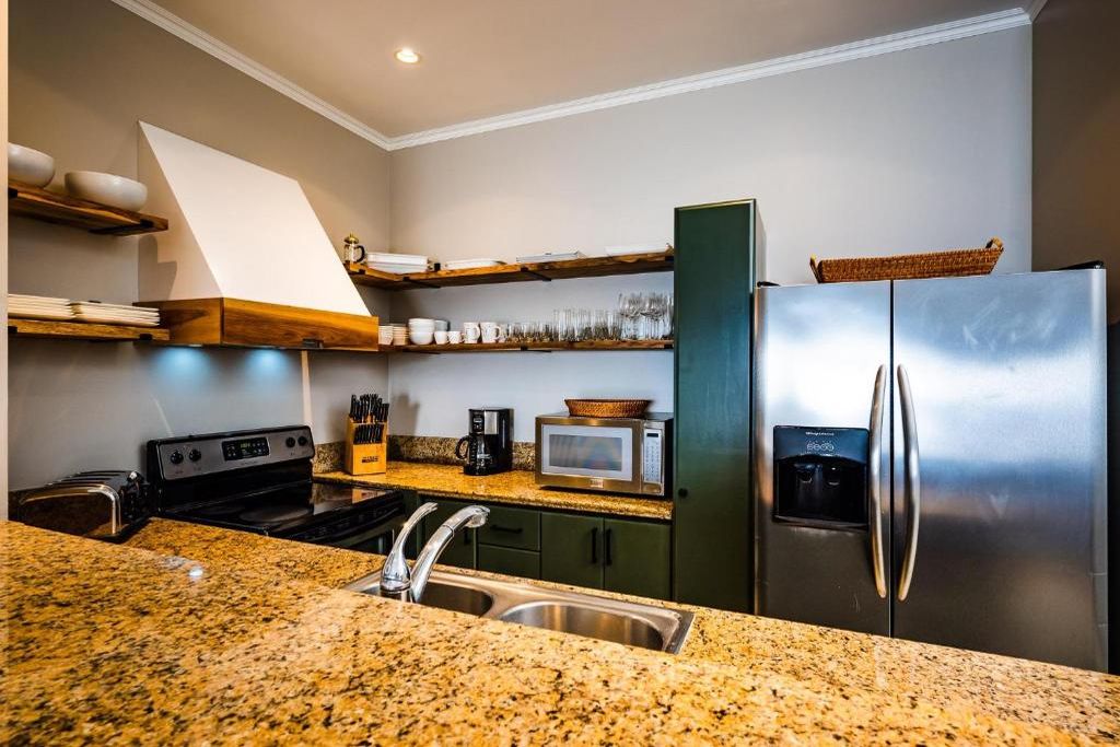 A kitchen with granite countertops, stainless steel appliances, and wooden shelves.