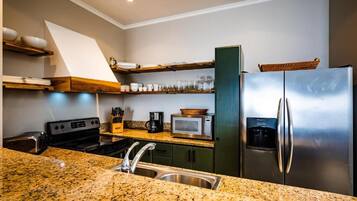 Cocina con encimeras de granito, electrodomésticos de acero inoxidable y estantes de madera.
