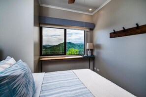 A bedroom with a large window, a bed, a bedside table, and a lamp.