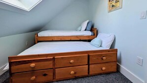 Um quarto com teto inclinado, claraboia, cama com duas almofadas e cómoda de madeira com gavetas.
