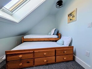 A bedroom with a sloped ceiling, a skylight, a bed with two pillows, and a wooden dresser with drawers. - Luxury Coastal Apt Above Bakery,Near Beach, Acadia (Hancock)