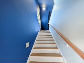 A staircase with white steps and wooden handrails, leading up to a landing with a light fixture. - Luxury Coastal Apt Above Bakery,Near Beach, Acadia (Hancock)