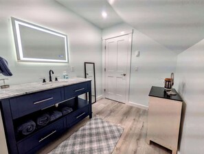 A modern bathroom with a vanity, a mirror, and a door. - Luxury Coastal Apt Above Bakery,Near Beach, Acadia (Hancock)