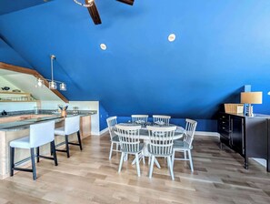 A modern kitchen with a blue ceiling, wooden flooring, and a dining area with white chairs. - Luxury Coastal Apt Above Bakery,Near Beach, Acadia (Hancock)