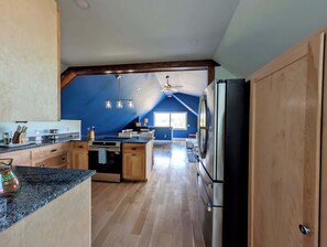 A modern kitchen with wooden cabinets, a granite countertop, a built-in oven, and a stainless steel refrigerator. - Luxury Coastal Apt Above Bakery,Near Beach, Acadia (Hancock)