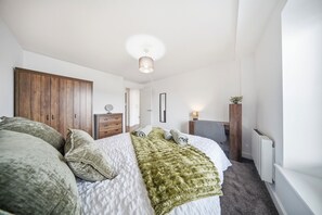 Ein Schlafzimmer mit Bett, Kommode, Spiegel, Heizkörper und Fenster.
