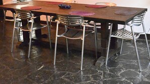 A rectangular dining table with six chairs, each with a metal frame and a mesh backrest. The table is set with a dark tablecloth, and there are two decorative plates on the table.