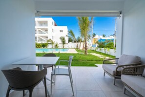 A patio with a table and chairs, a sofa, and a view of a swimming pool and buildings. - Cabarete Apt I Direct Pool Access (Cabarete)