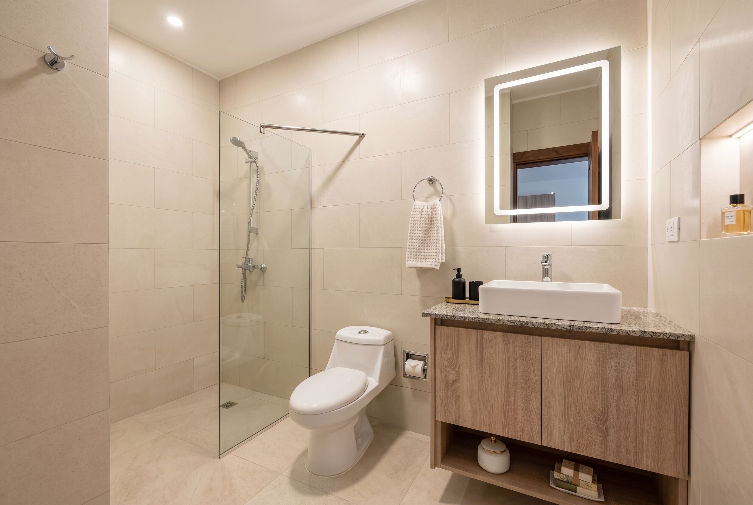 Ein modernes Badezimmer mit einer gläsernen Duschkabine, einer weißen Toilette, einem Waschtisch mit Spiegel und einem Waschbecken.