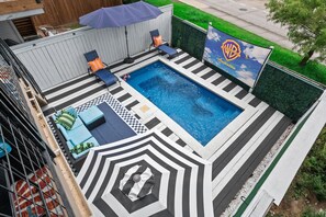 A swimming pool with a checkered deck, lounge chairs, and a Warner Bros. Pictures banner. - Wonderland in East Downtown - Pool! (Houston)