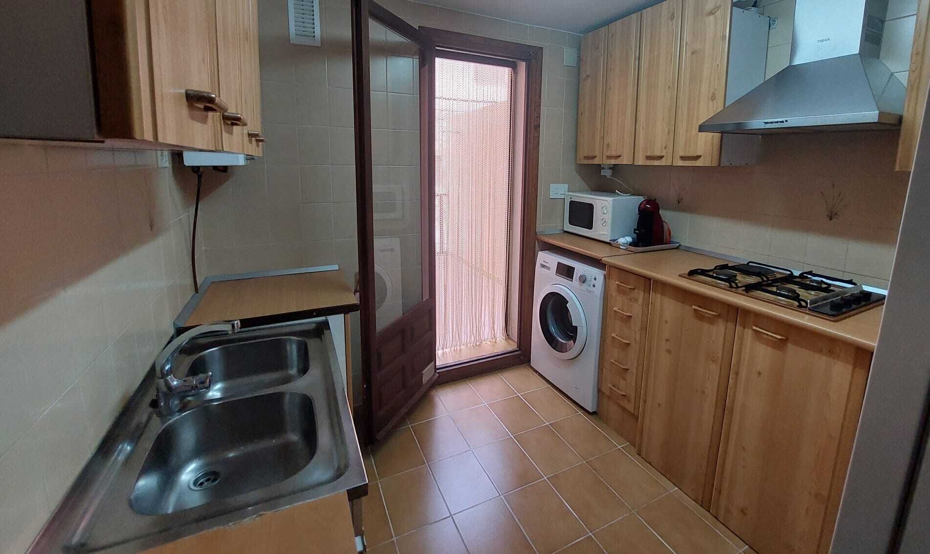 Une cuisine compacte équipée d’un évier, d’un lave-linge, d’un four à micro-ondes et d’une cuisinière à gaz.