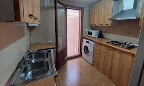 A compact kitchen with a sink, washing machine, microwave, and a gas stove.