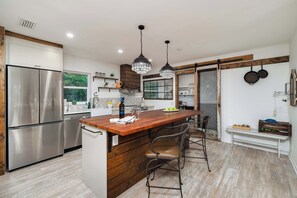 Une cuisine moderne avec un îlot central en bois, des appareils électroménagers en acier inoxydable et des luminaires suspendus.