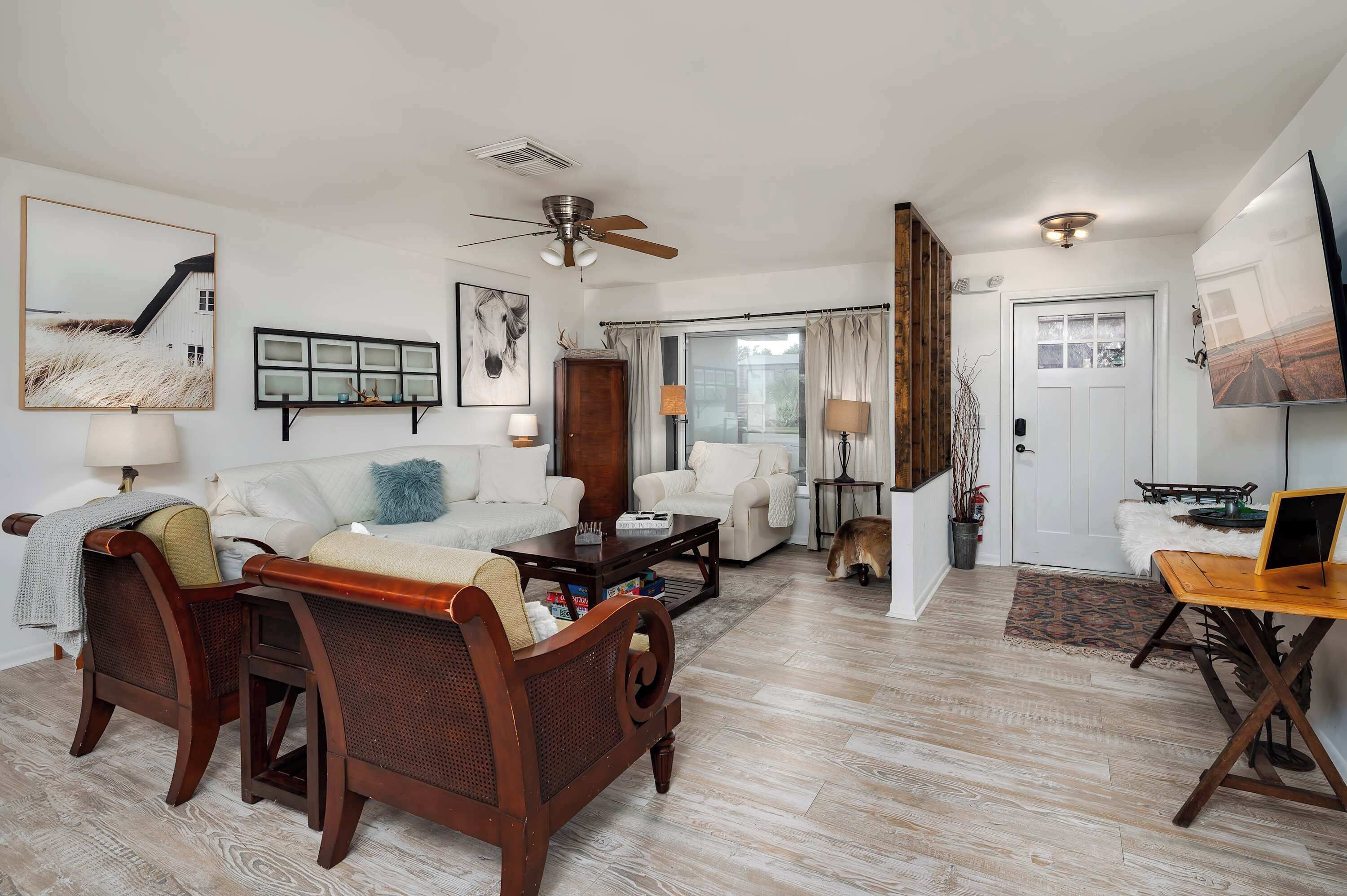 A spacious living room with a sofa, coffee table, and a wooden chair. There is a ceiling fan, a fireplace, and a door leading to another room.
