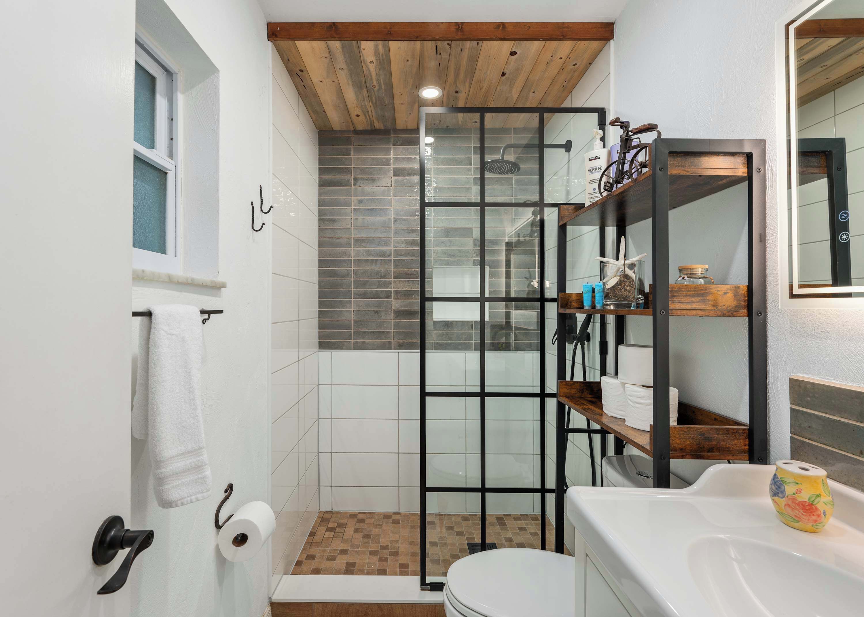 A bathroom with a shower enclosure, a toilet, a sink, and a wooden ceiling.