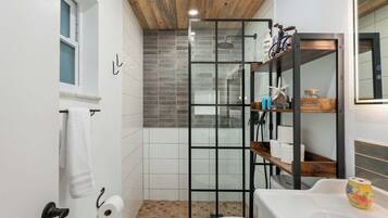 A bathroom with a shower enclosure, a toilet, a sink, and a wooden ceiling.