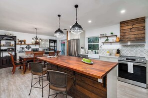 Une cuisine moderne dotée d’un îlot central, d’appareils électroménagers en acier inoxydable et de luminaires suspendus.