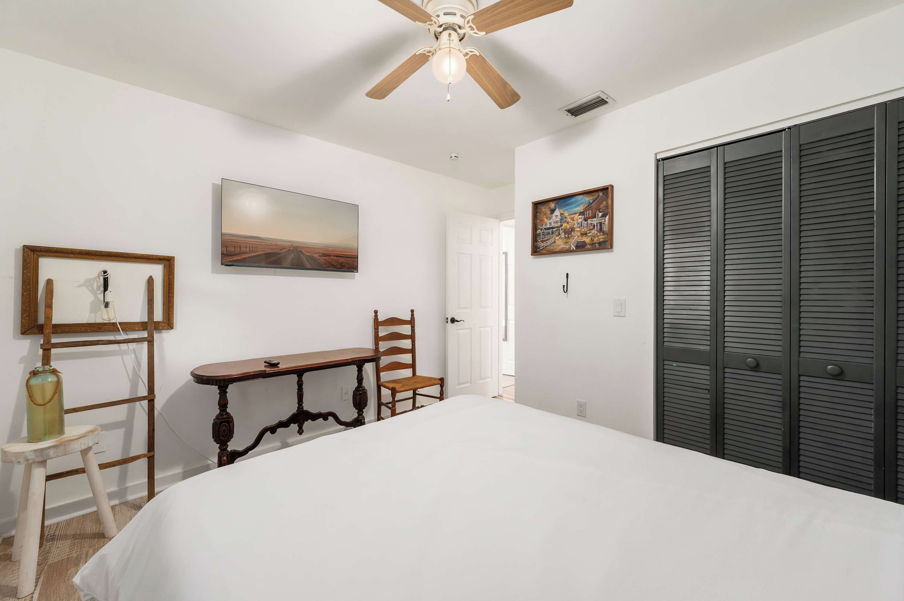 Une chambre à coucher comprenant un lit, un bureau, une chaise, un ventilateur de plafond et une armoire.
