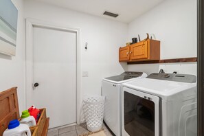 Une buanderie équipée de deux machines à laver, d’un sèche-linge, d’un meuble en bois et d’un panier contenant des produits de nettoyage.