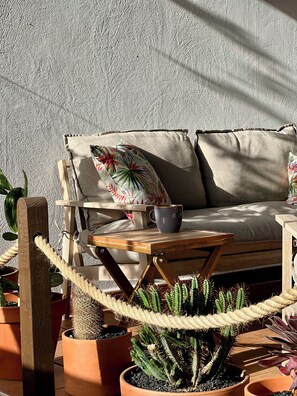 Un espace extérieur accueillant, aménagé avec un canapé, une table en bois et divers pots de plantes, notamment des cactus.