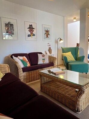 Een zithoek met een bank, een groene fauteuil, een rieten salontafel en wanddecoratie.