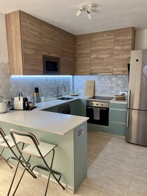 A modern kitchen with wooden cabinets, a stainless steel refrigerator, and a central island with bar stools. - Private Villa with Roof Terrace & Mountain Views (Yaiza)