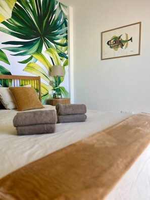 Een net opgemaakt bed met een bruine deken, een houten hoofdbord en een grote wand met tropische planten.