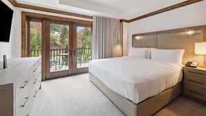 Une chambre d’hôtel avec un grand lit, un bureau, une chaise et un balcon offrant une vue sur les immeubles et les arbres.