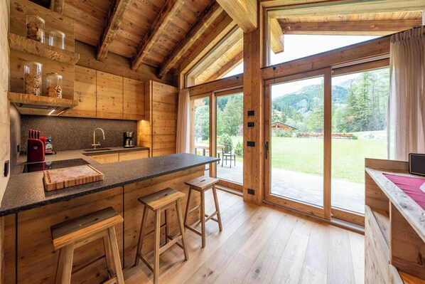 A wooden cabin kitchen with a large island, bar stools, and a view of the outdoors.