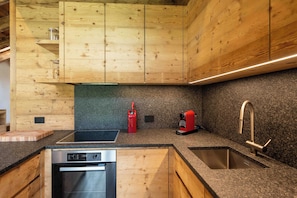 A modern kitchen with wooden cabinets, a built-in oven, a coffee machine, and a stainless steel sink.