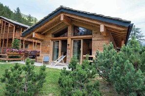 A wooden cabin with a sloped roof, large windows, and a deck area with outdoor furniture.