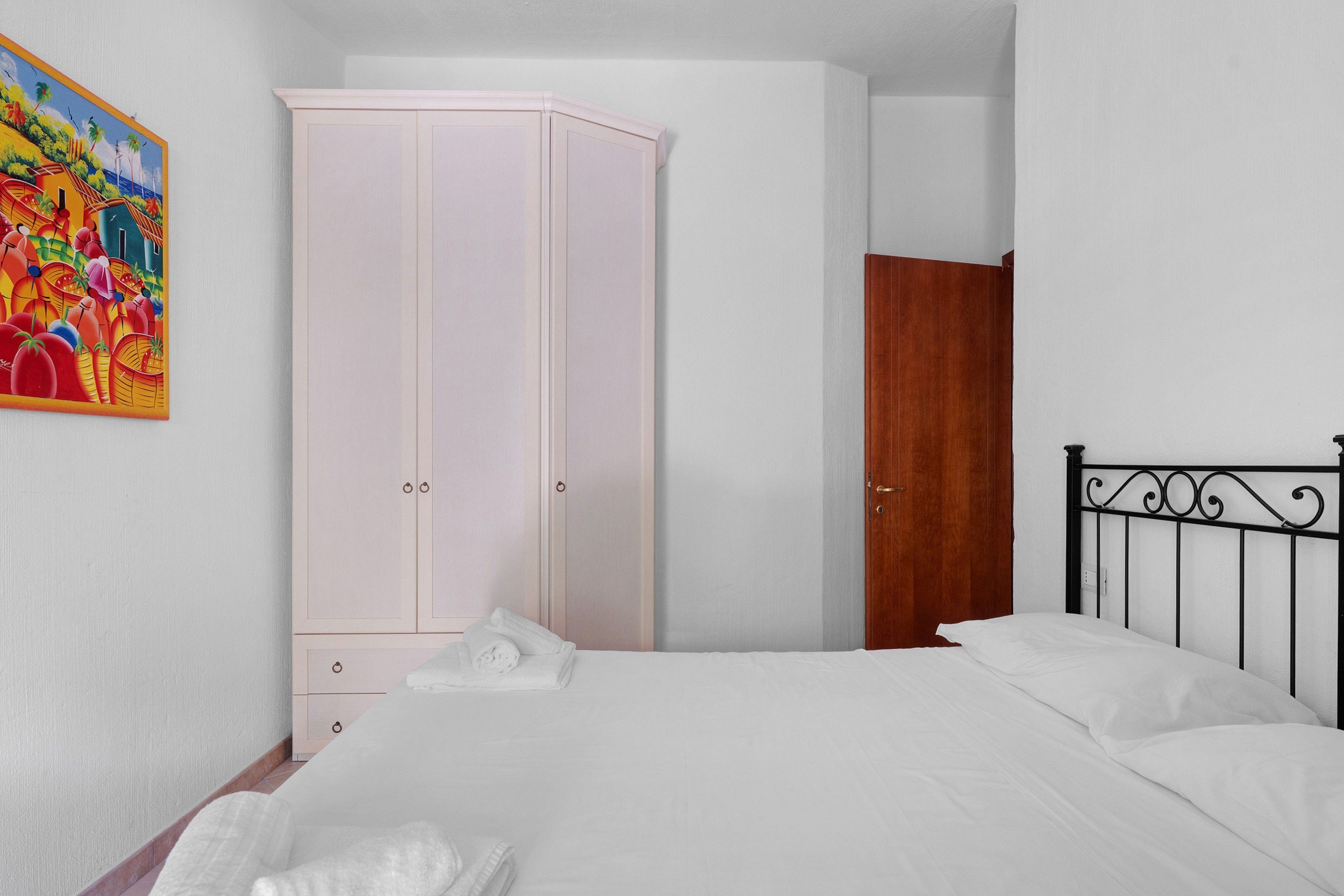 A bedroom with a bed, a wardrobe, a wooden door, and a painting on the wall.