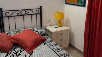 A bedroom with a bed, a nightstand with a lamp, a painting on the wall, and a red curtain.