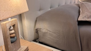A neatly made bed with a headboard, a bedside table with a lamp, and a small wooden sculpture on the table.