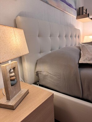 A neatly made bed with a headboard, a bedside table with a lamp, and a small wooden sculpture on the table.