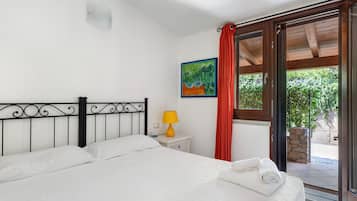 A bedroom with a bed, a nightstand, a lamp, a painting, and a view of the outdoors.