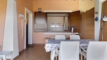 A dining area with a table and chairs, a window with blinds, and a ceiling with wooden beams.