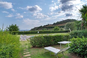 Un jardín con piscina, sillas de descanso y vistas al mar.
