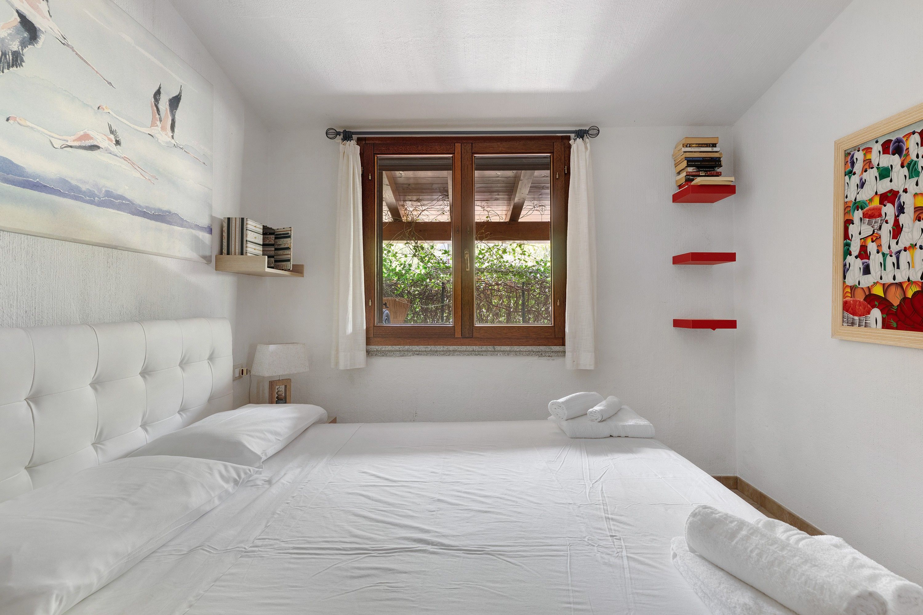 Ein Schlafzimmer mit Bett, Fenster, einem Gemälde und einem Bücherregal.