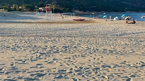 A beach with a mountain in the background, a lifeguard tower, and people enjoying the beach.
