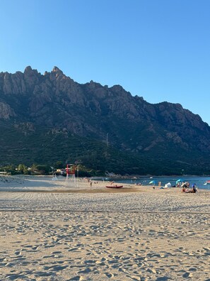 A beach with a mountain in the background, a lifeguard tower, and people enjoying the beach.