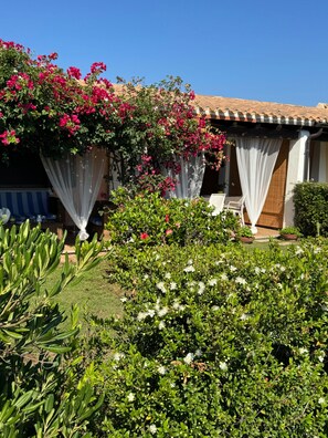 A house with a garden, a patio with a table and chairs, and a covered area with curtains.