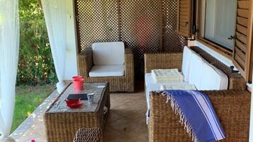 A covered outdoor seating area with wicker furniture, a table with cups, and a view of greenery.