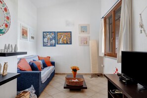 A living room with a sofa, a coffee table with flowers, a TV, and artwork on the wall. - Villino Empatja: an emerald sea at your doorstep (Tertenia)
