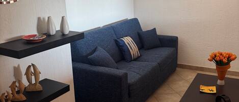 A living room with a blue sofa, a coffee table, and artwork on the walls.