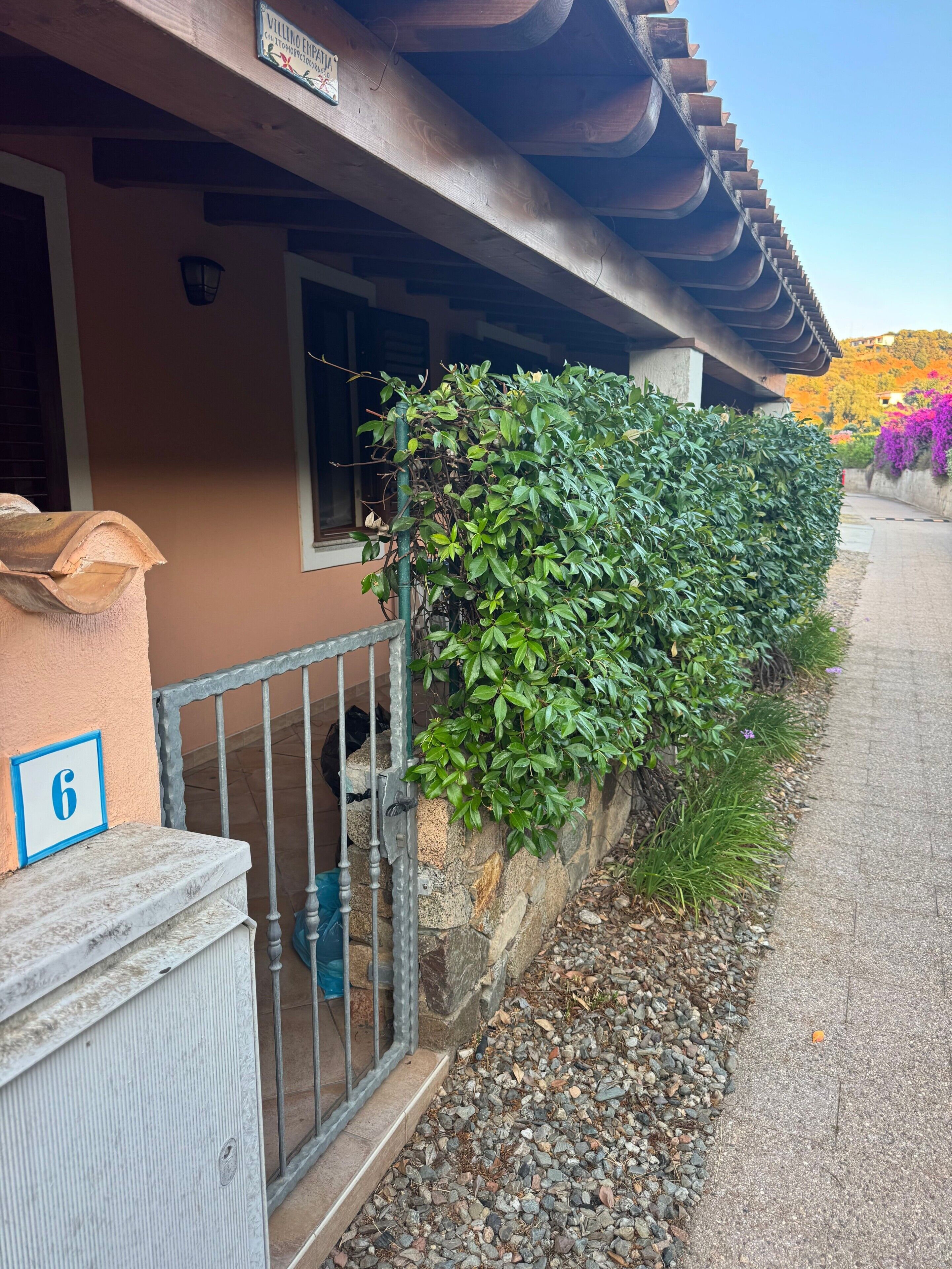 A building with a stone wall, a metal gate, and a number sign indicating room 6.
