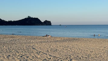 A sandy beach with footprints, a calm sea, and a distant rocky outcrop.